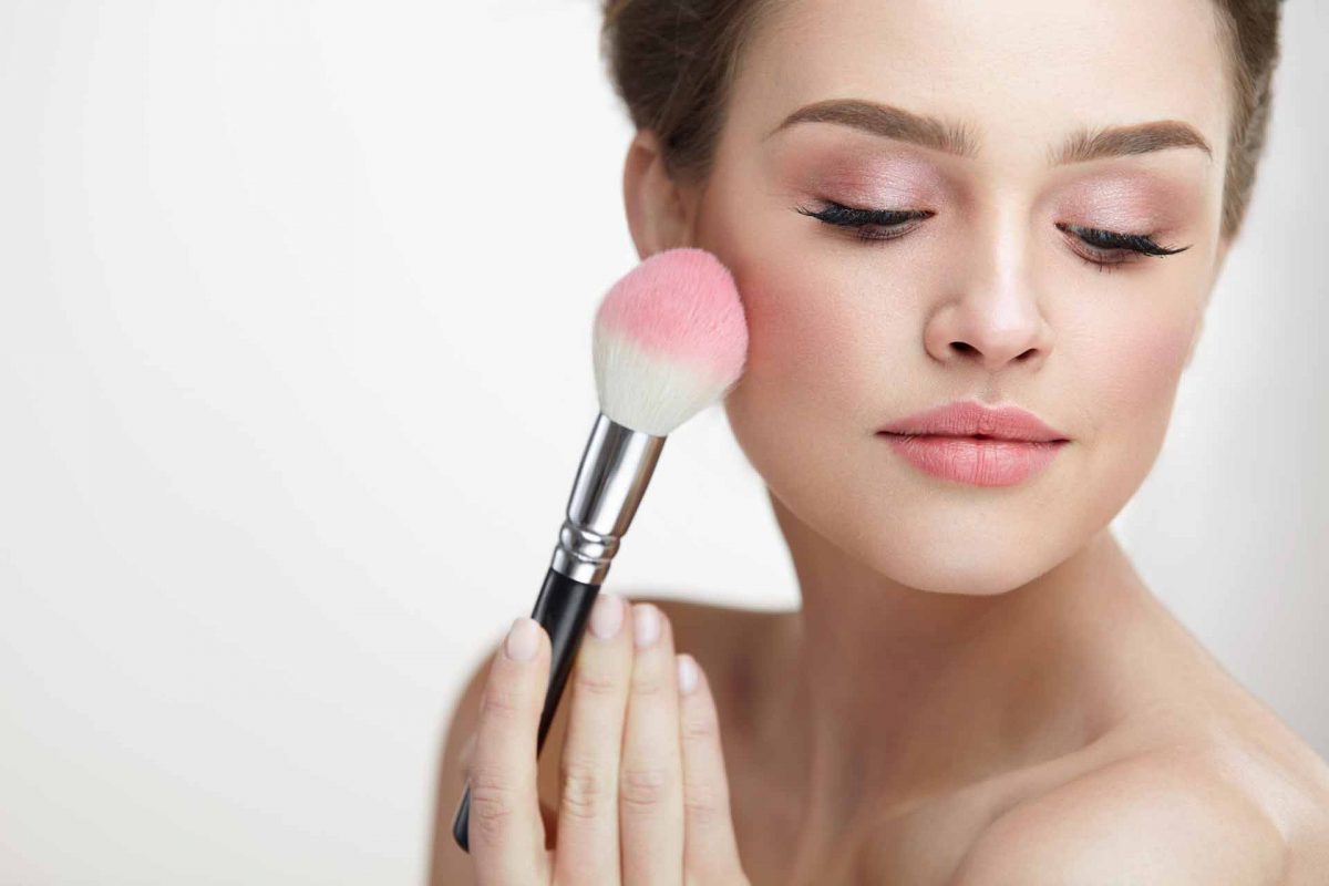 Facial Beauty Cosmetics. Portrait Of Attractive Female With Pure Soft Skin Applying Pink Loose Blush On Face. Closeup Of Beautiful Sexy Woman With Fresh Makeup Holding Cosmetic Brush. High Resolution